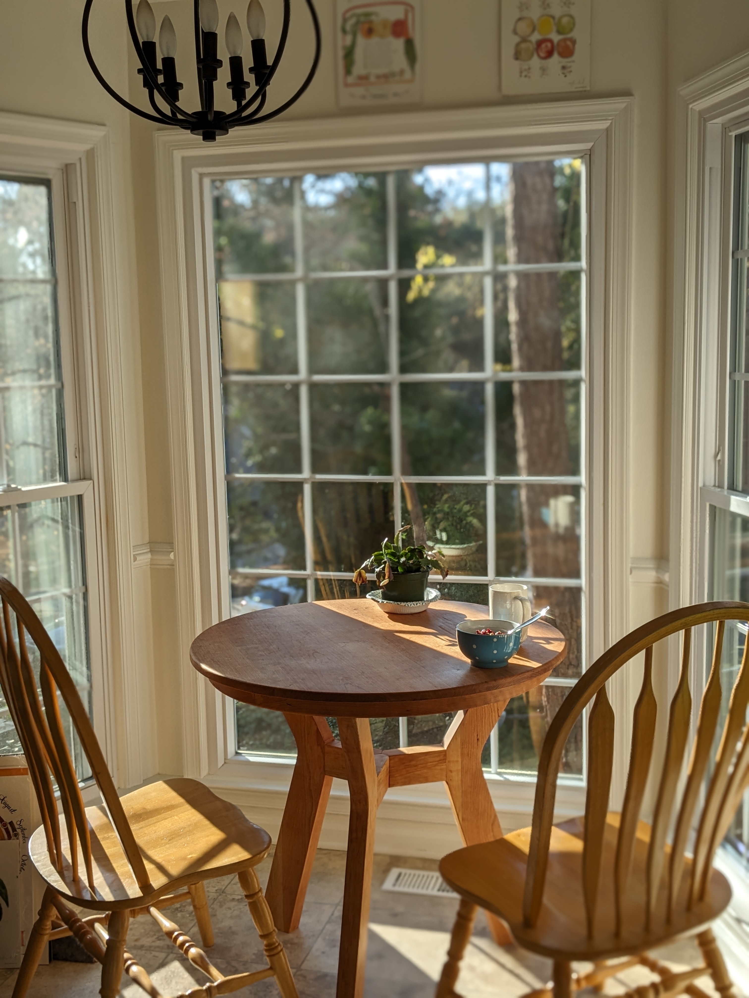 A round cherry dining table with three legs, in a breakfast nook, with tea on it
